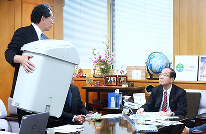 原田義昭環境大臣（右）とリサイクルボックスを手に説明する中田雅史専務理事