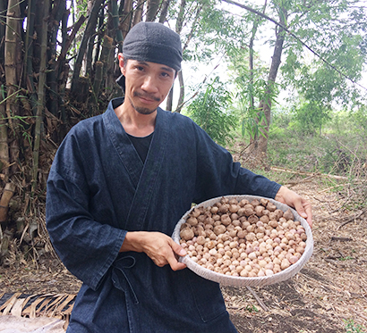 「忍の森」の前で、熟成を終えた黒ニンニクを持つ宮内靖彦さん=提供写真