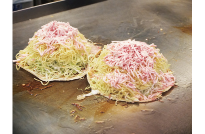 薄く生地を敷き、キャベツ、麺、ひき肉をのせ、ひっくり返して鉄板に押しつけるように焼くと、パリパリ食感の新感覚お好み焼きが完成する