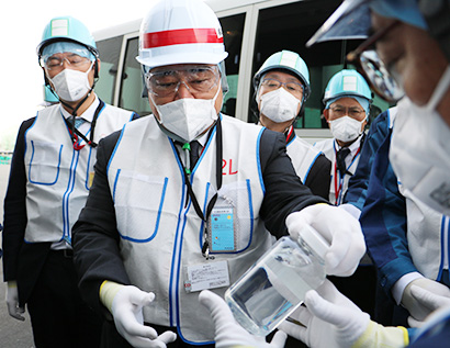 高性能ALPS前で説明を受け10月29日に採取した処理水を手にする梶山弘志経産相。ALPSの62核種の除去性能をモニタリングするため、こうしたサンプルを1週間に2回採取しているという=記者団代表社撮影