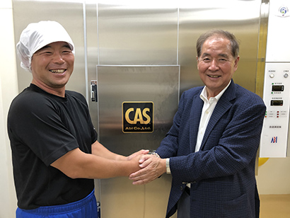 CASエンジン付急速凍結機の前で握手する漁師の浦谷俊晴さん（左）とアビーの大和田哲男社長