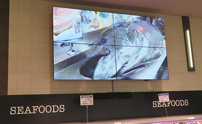鮮魚売場の壁面に大型のデジタルサイネージでマグロの解体ショーを配信