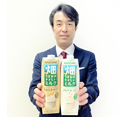 「畑うまれのやさしいミルク」（1000g）を手にする鶴田秀朗飲料企画部長