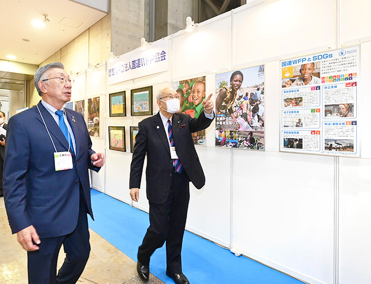 ファベックス展の国連WFP協会ブースを視察する安藤宏基会長とパネル展示を説明する日本食糧新聞社・今野正義会長CEO