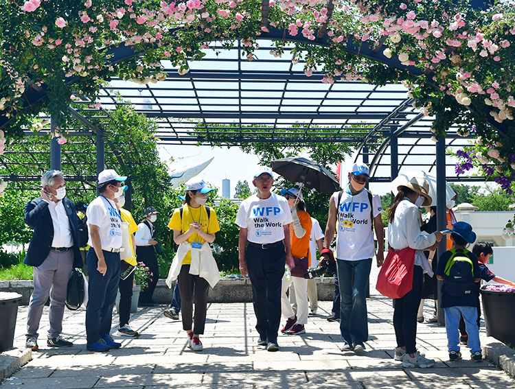 満開のバラ園をウオーキングする安藤宏基会長（手前左から4人目）