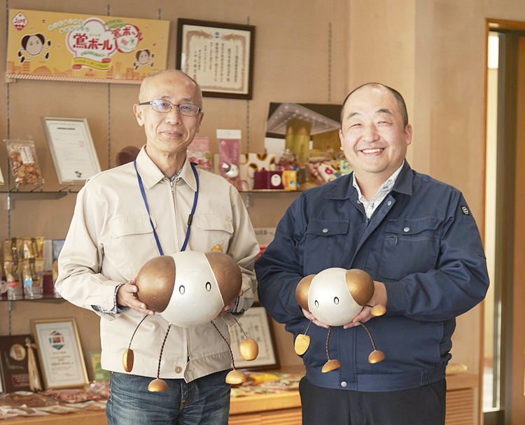 植垣清貴植垣米菓代表取締役（左）と伊賀弘同総務部長。同社キャラクターかりんちゃん、こりんちゃんと一緒に