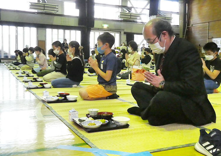 11月21日の新宿区立津久戸小学校での和食給食、講堂でござを敷いて牧田健一校長（手前）と一緒に食べた