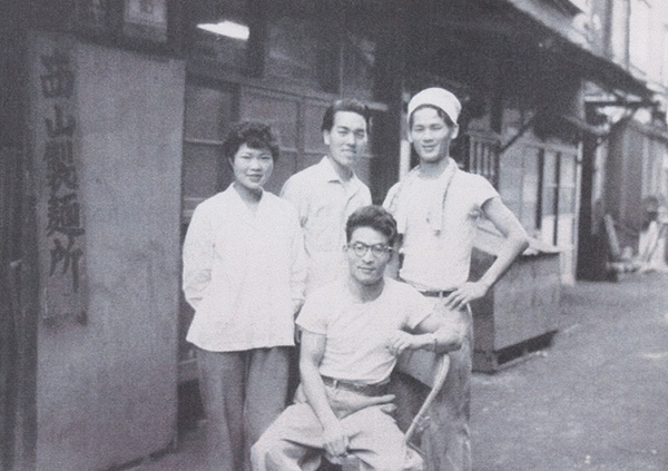 昭和28年開業した「西山製麺所」前で従業員と記念撮影する西山孝之氏（中央）